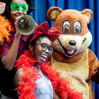 First year students pose for a photo with a bear mascot, feather boas and face masks