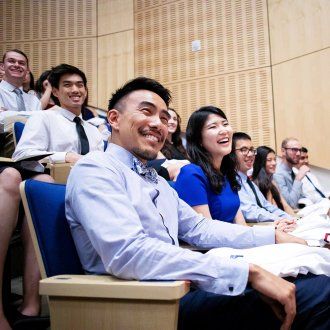 During the School of Pharmacy white coat ceremony a row of students laughs while a speaker presents