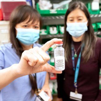 Two pharmacists wearing masks hold up a bottle of remdesivir during the COVID-19 pandemic