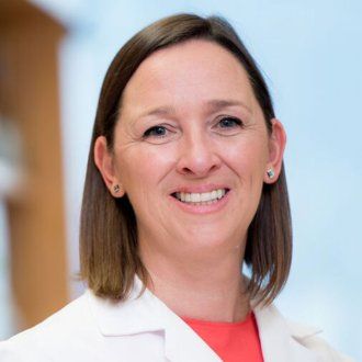 Susan Lynch poses for a headshot in her lab wearing a white lab coat.