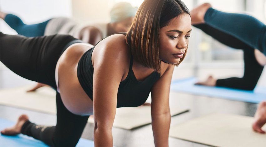 A young Black pregnant woman does exercises on a yoga mat along with other women