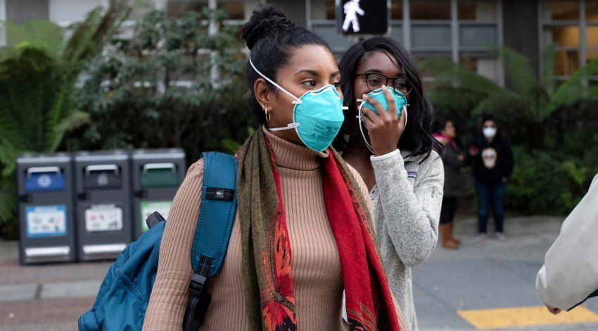 Two Black women stand outside wearing blue N95 face masks.