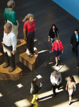 Individuals walk by a sculpture of different people in the Rutter Center