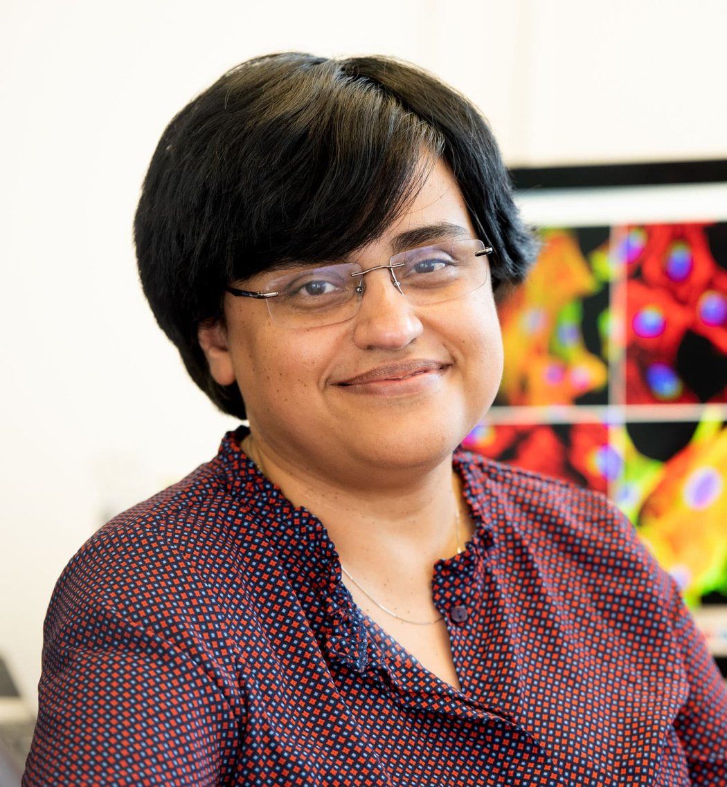 Shaeri Mukerjee sits in her office. Behind her is a monitor with microscopic images