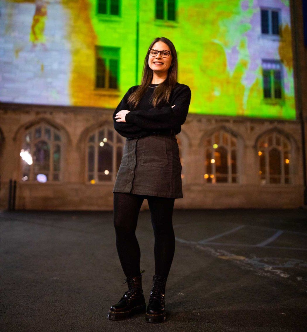 Katina Bitsicas stands in front of a building with digital media projected onto its facade.