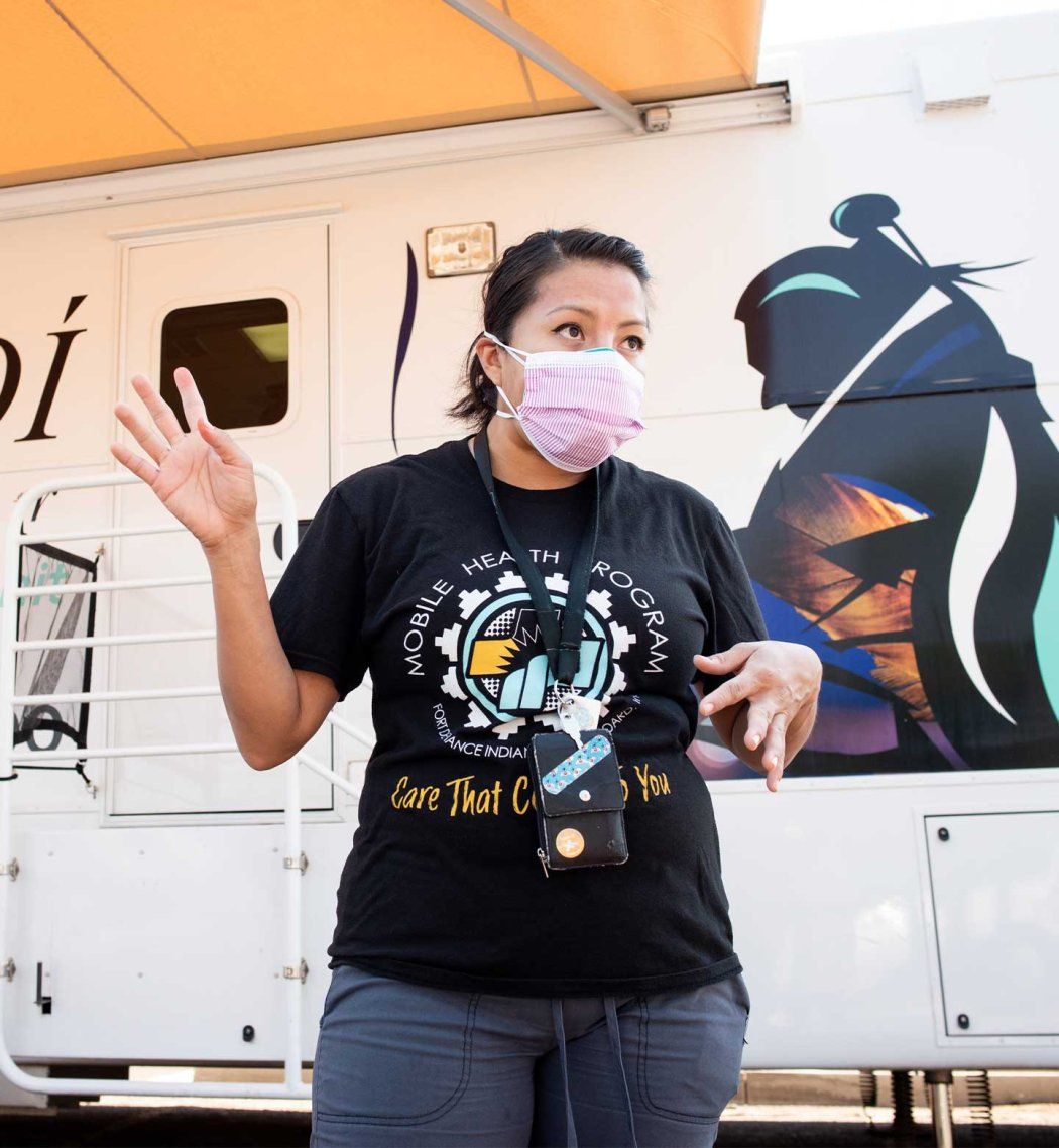 An indigenous woman wearing a surigcal mask stands outside a mobile clinic while talking to a patient in Ford Defiance.