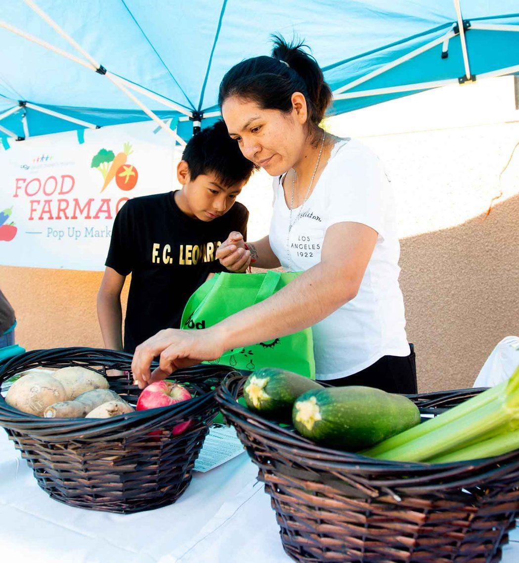 A Latino mother and her son collect fresh vegetables at a food clinic.