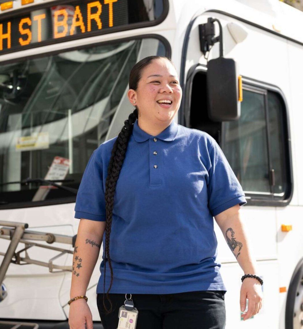 shuttle driver stands in front of bus smiling