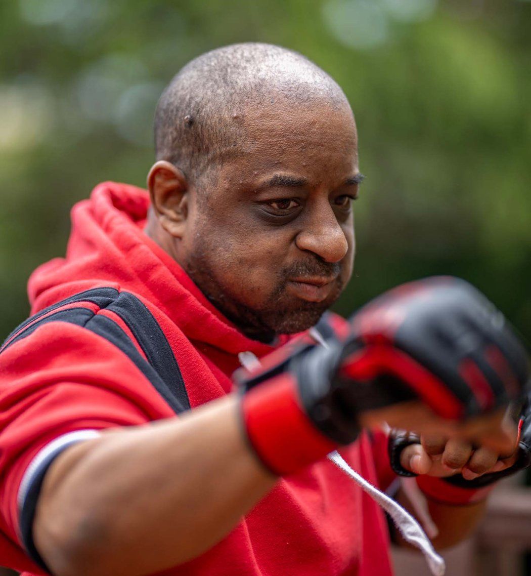 Patient Russell Hughes spars while wearing boxing gloves and a red hoodie.