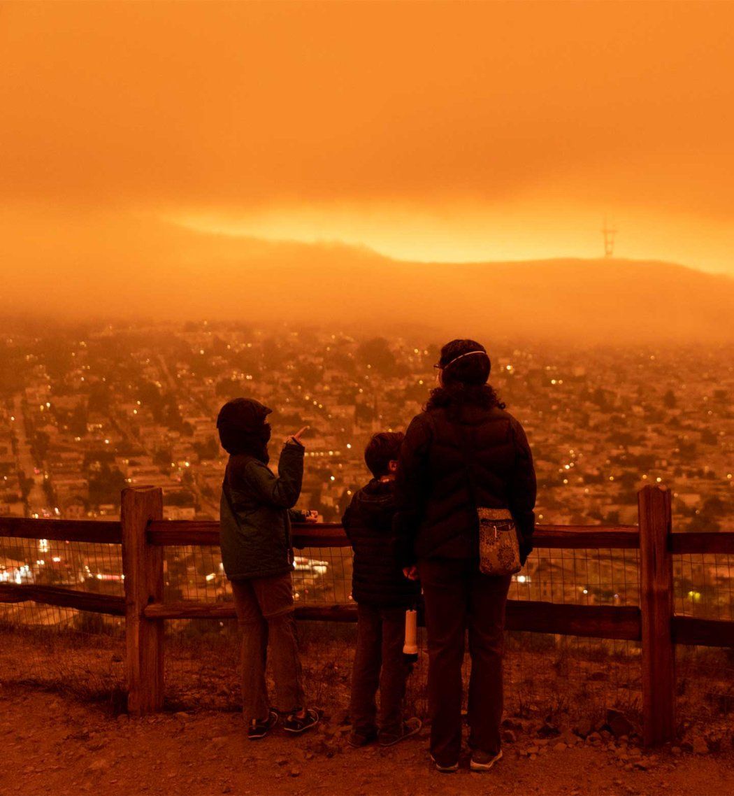 Two children and their mother wear facial masks as they look out at orange wildfire smoke.