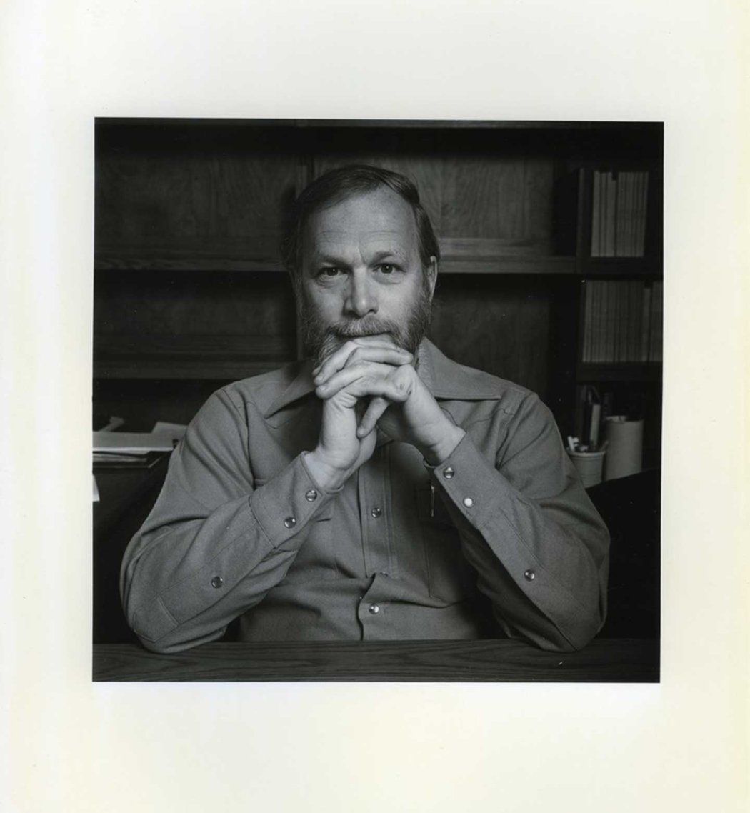 A black and white polaroid of J. Michael Bishop sitting at his desk.