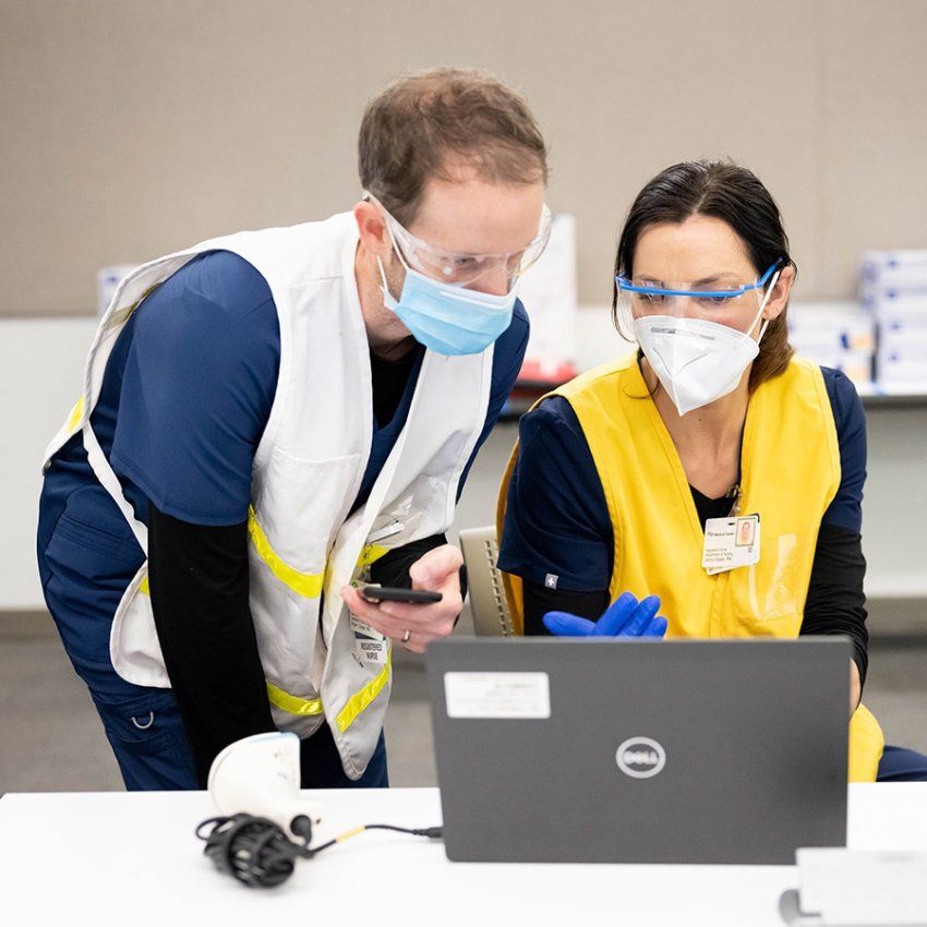Two staff members looking at a laptop at a vaccination site for COVID-19