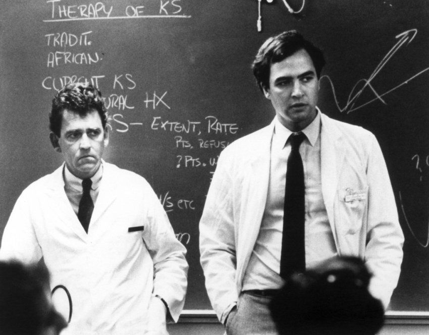Marcus Conant and Paul Volberding stand in a classroom in front of a chalkboard while they discuss Kaposi's Sarcoma