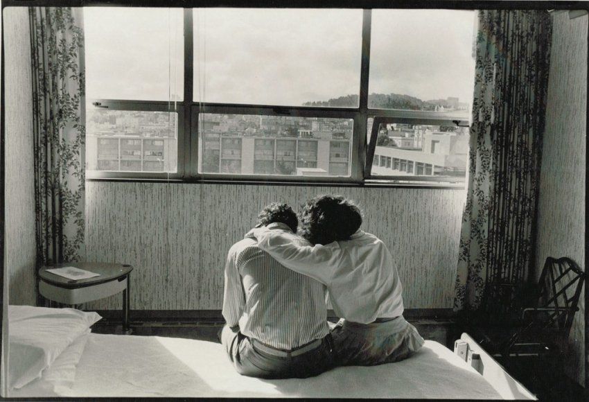 A man and a woman embrace on a bed as the afternoon light falls through the window
