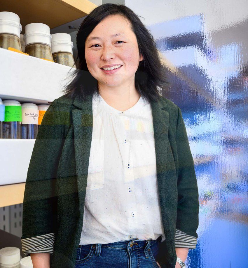 Qili Liu stands and smiles against an abstract backdrop of research imagery