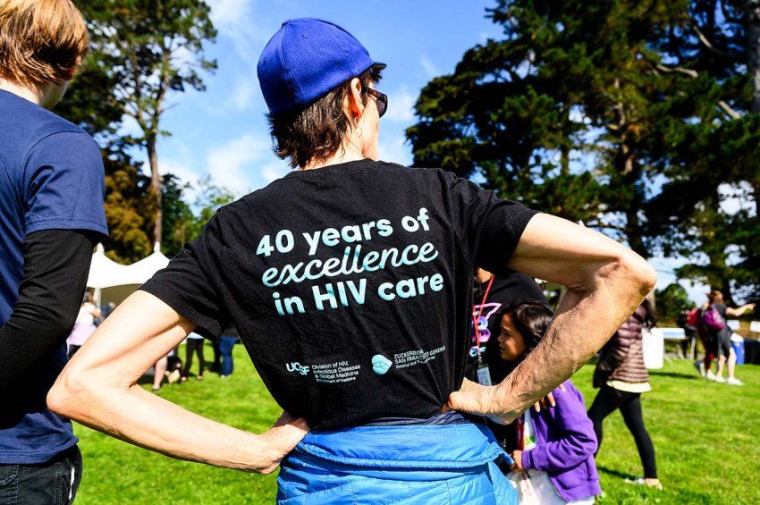 A woman turns away from the camera to show the back of her shirt, which reads "40 Years of Excellence in HIV Care."