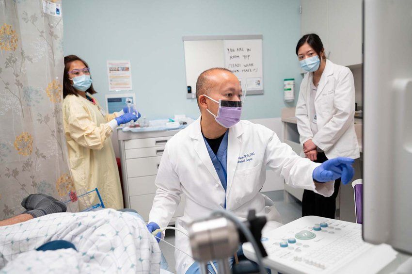 Hao Nguyen takes an MRI of a prostate in an exam room while two medical staff members stand in the background ready to help.